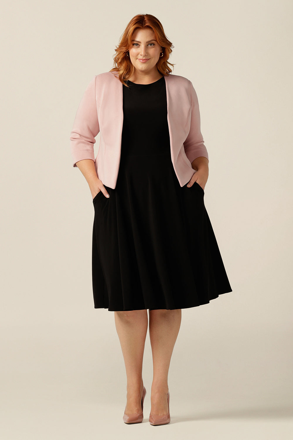 a size 18, plus size woman wears a collarless, open-front pink jacket with 3/4 sleeves. Made in Australia from stretch modal, a sustainable natural fibre, this is an eco-conscious quality corporate jacket. The sustainably-produced women's jacket is style with a black jersey dress for classic smart work style.