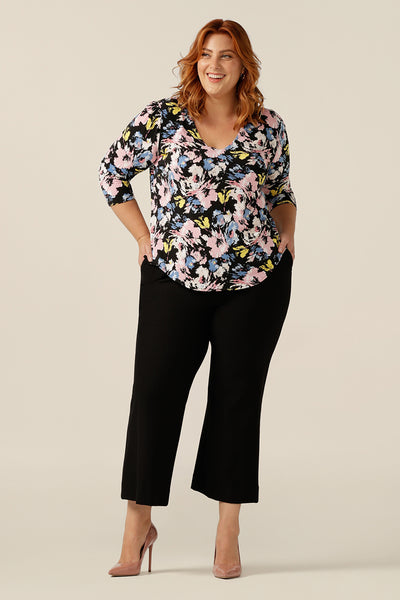 a curvy size 18 woman wears a V-neck top with 3/4 sleeve. In pastel colours, a vintage floral print patterns this jersey top's stretch fabric. Worn with black wide-leg pants, this top is styled as work wear top, with a smart-casual look. Made in Australia, this quality top for work or casual wear, is designed to fit women from sizes 8 to size 18.