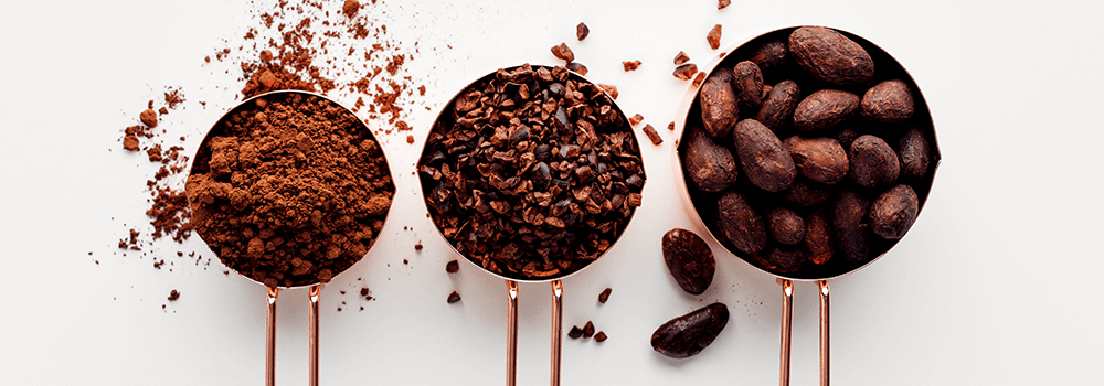 3 metal measuring cups with cacao beans, nibs and power in them