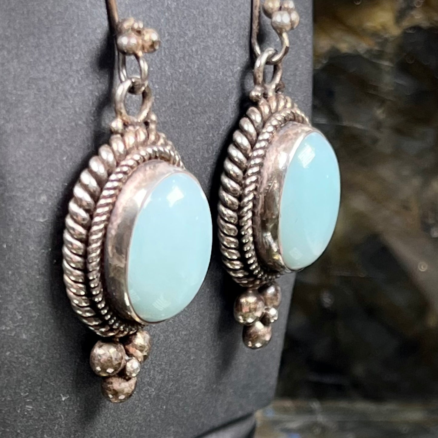 A pair of silver wire dangle earrings set with blue agate stones. The earrings have a braided rope design.