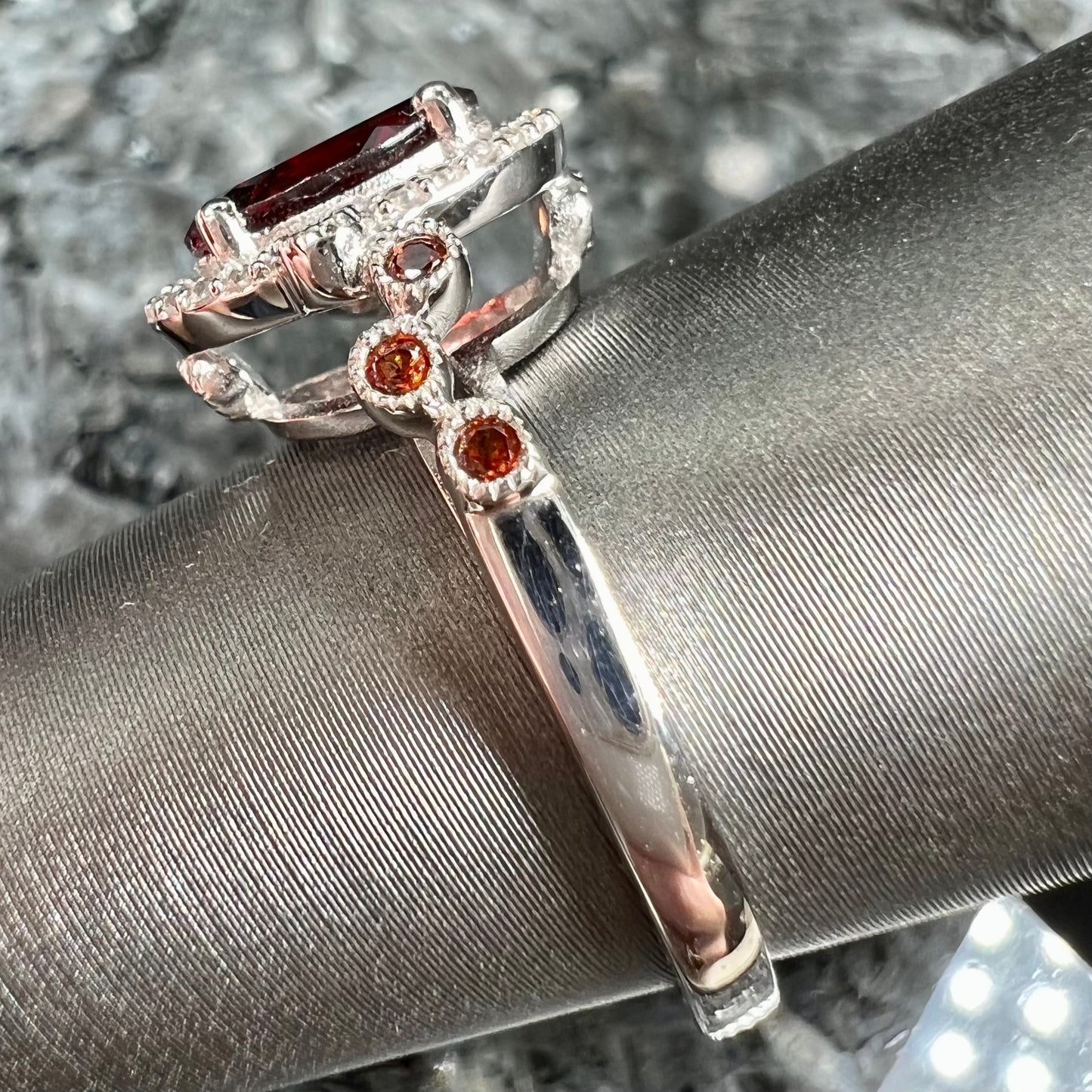 A silver garnet and CZ halo ring. The center stone is a red almandine garnet, and the side garnets are orange.