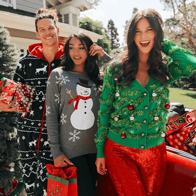 shop christmas - image of man wearing blue reindeer jumpsuit next to two women wearing sequined snow day ugly christmas sweater and the other wearing gaudy garland ugly christmas cardigan and high waisted red sequined leggings