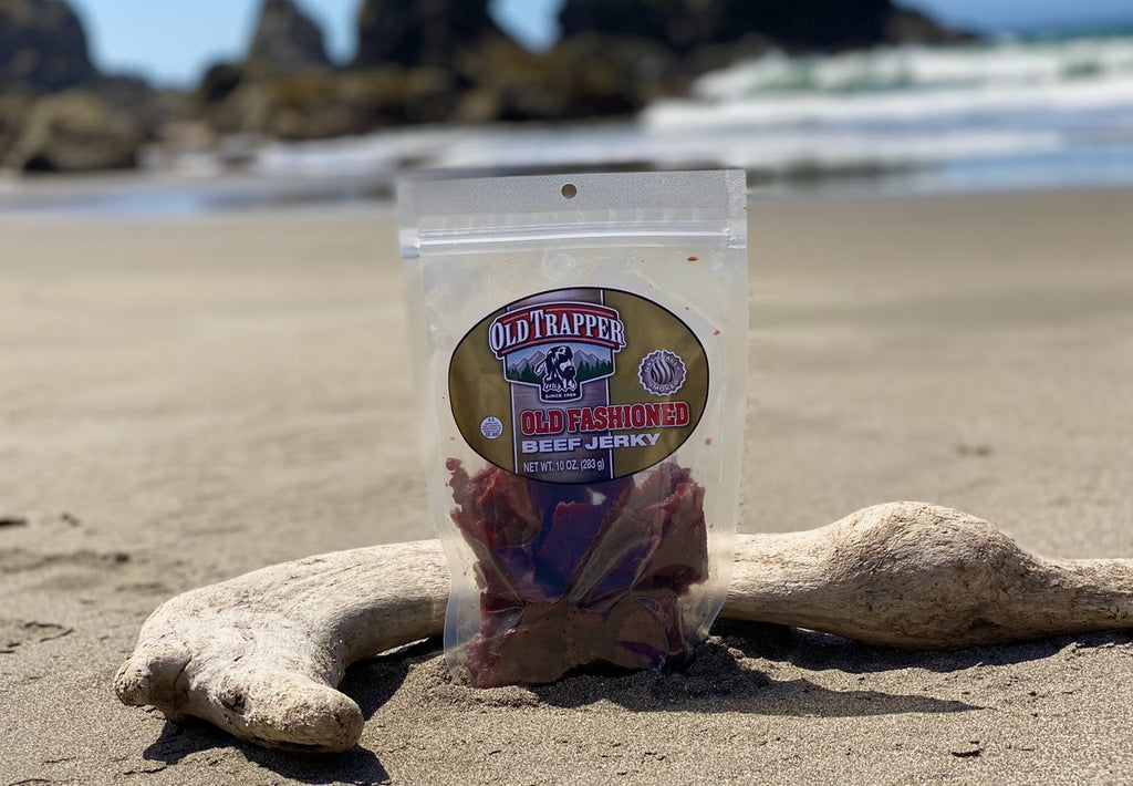 Old Fashioned Beef Jerky bag resting against a piece of driftwood on the beach.