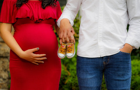 Pregnant mom &amp; dad posing for a picture with baby shoes