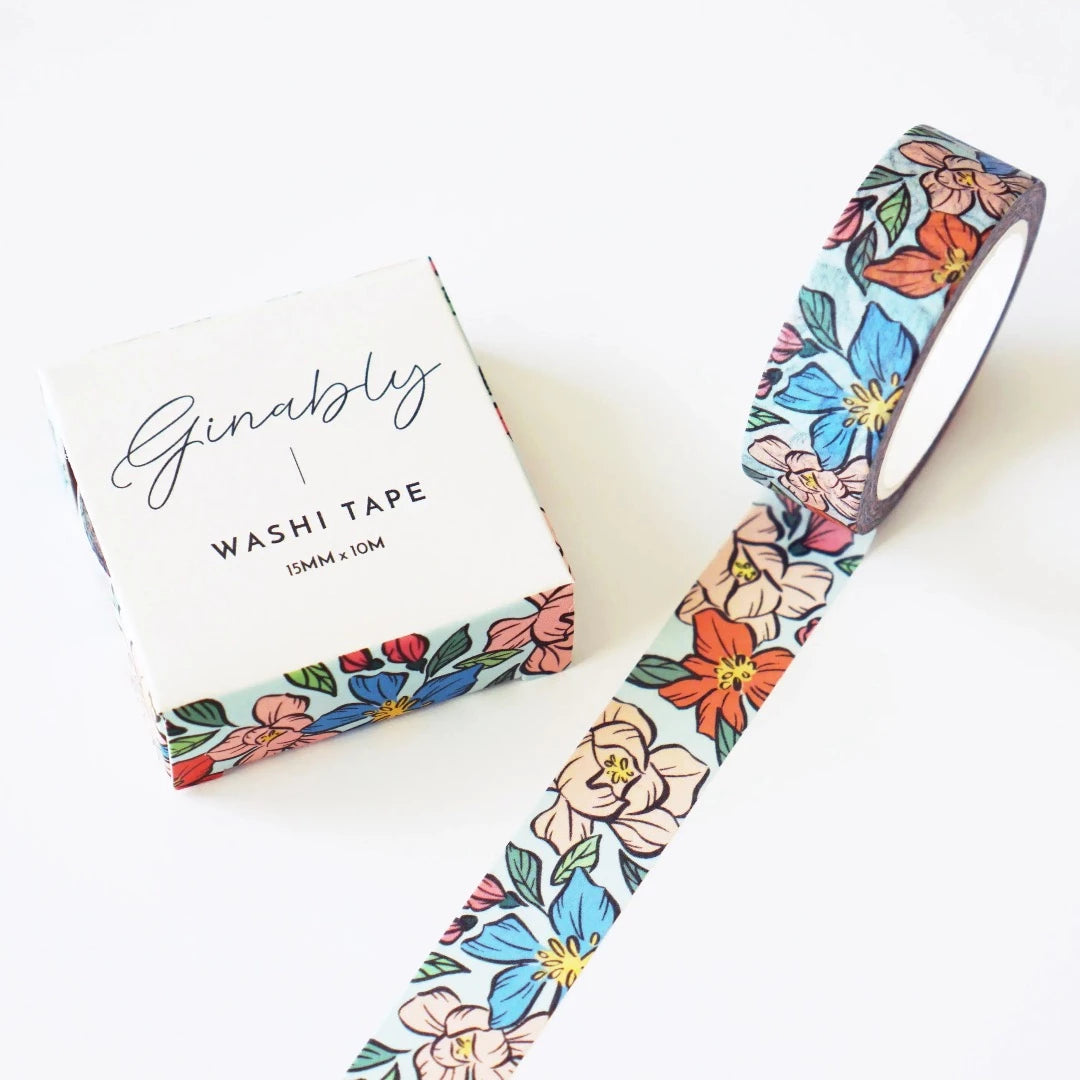 light blue washi tape with multicoloured flowers all over it and it's sitting next to it's original packaging which has the same design on it except for the top which is white and says ginably and washi tape on it