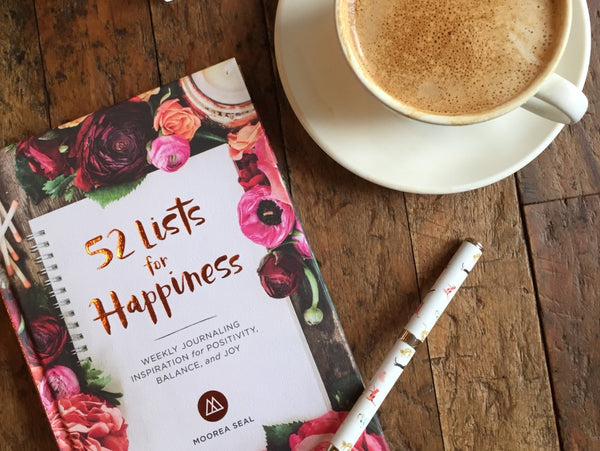 Flat lay of 52 Lists for Happiness on a wooden table with a latte in soft morning light