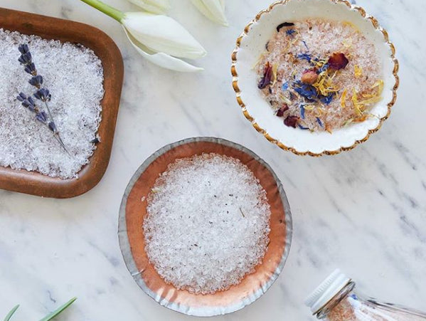 Flatlay of three ceramic bowls containing Dot and Lil bath salts with dried flowers on a marble counter.