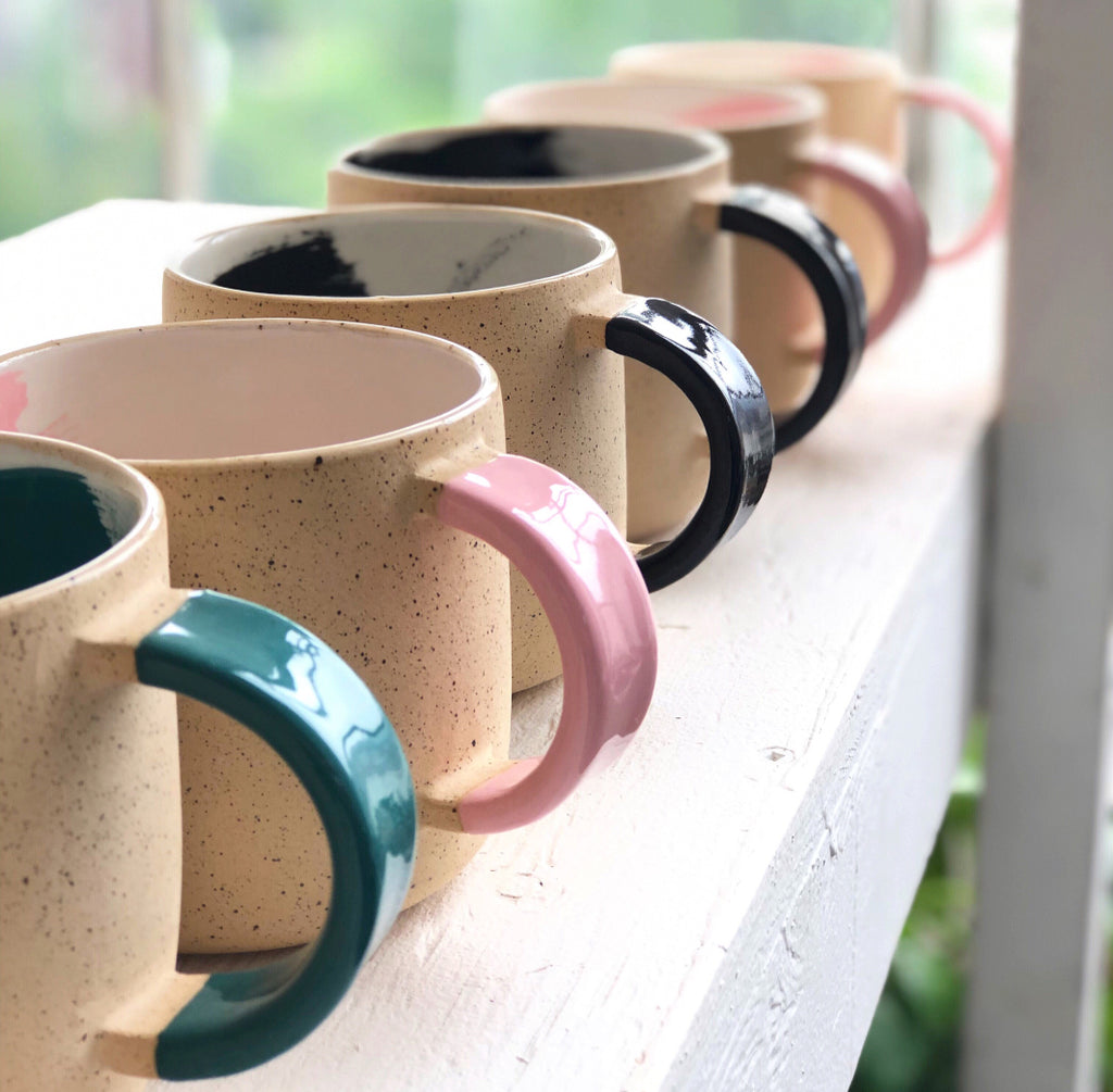 Line-up of Shayna Stevenson's signature ceramic brushstroke mugs in green, black, and pink