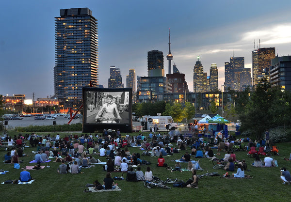 Crowd of people sitting on the grass in a park, watching an outdoor film screening in Toronto