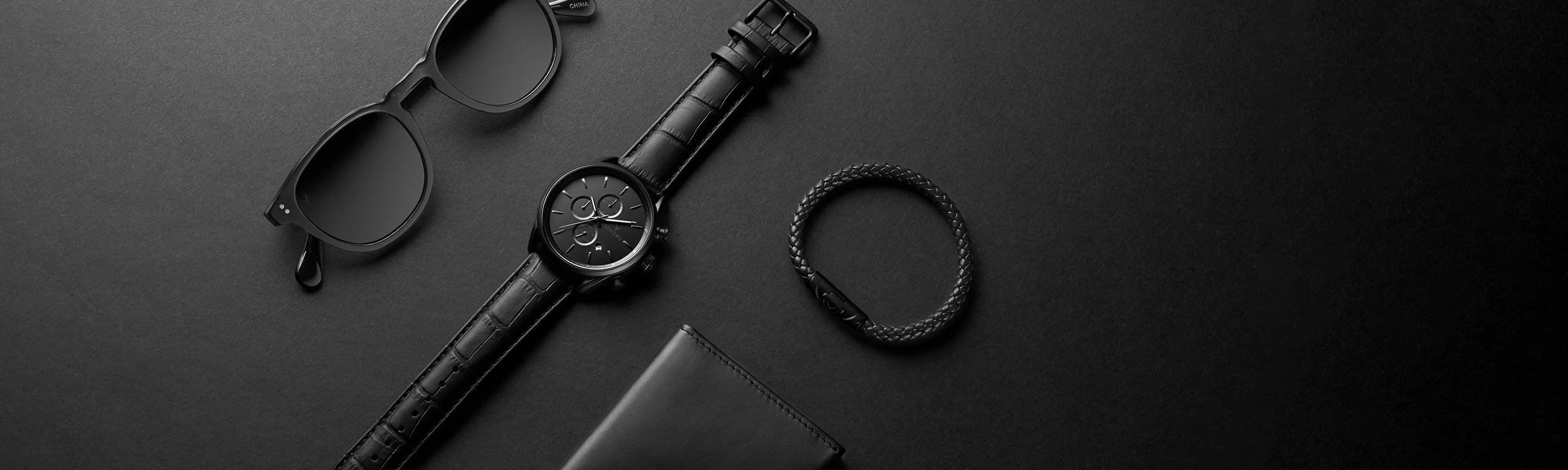 Black sunglasses, watch, and bracelet in matte black background