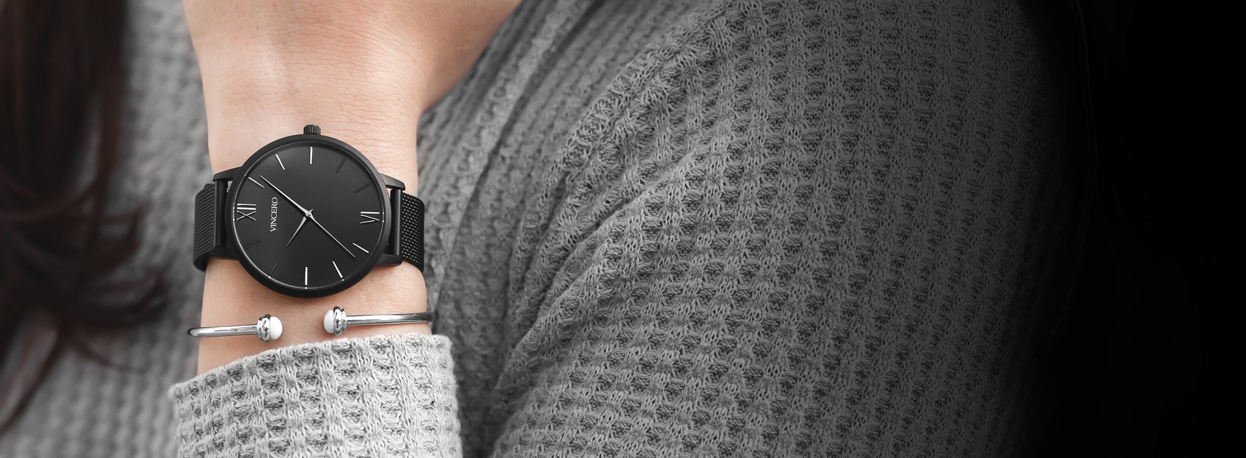 Woman in grey sweatshirt with matte black watch and silver cuff bracelet