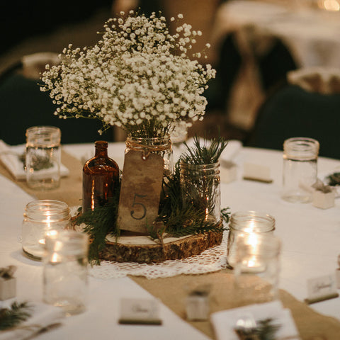 Wedding table decor with a rustic centrepiece featuring mason jars and baby's breath and mason jars as drinking glasses