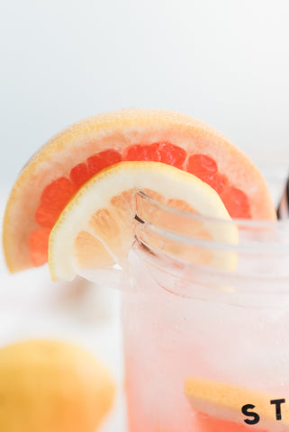 fresh slice of lemon and grapefruit on the edge of a glass mason jar full of pink lemonade