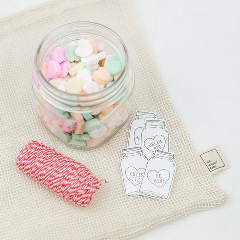 decorative red twine and valentines gift tags next to a wide mouth mason jar filled with valentine's candy