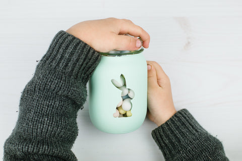 small child's hands holding an aqua painted mason jar with a bunny silhouette and full of mini eggs