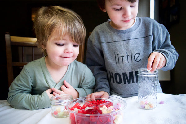 two young boys filling mason jars with their favorite valentine's candies
