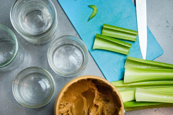 knive on a blue cutting board next to bright green celery and peanut butter and a row of empty mason jars