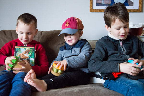 three boys opening brightly coloured mason jars filled with celery sticks and peanut butter