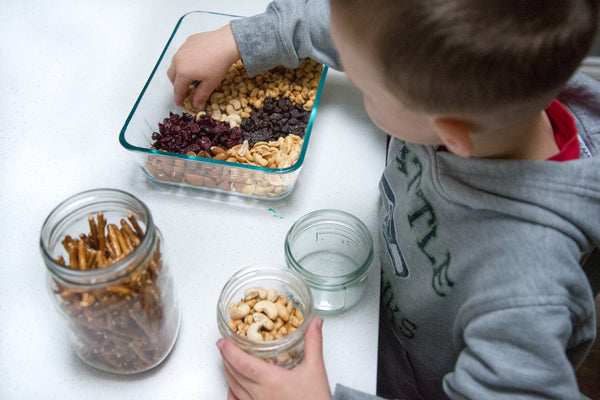 a young boy mixing various nuts and other salty snacks into a jar