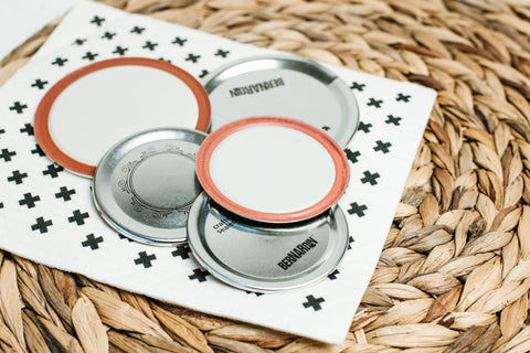 a small pile of flat canning lids in regular and wide mouth sizes on top of a black and white sponge cloth