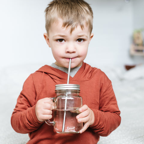 small children drinking water from a reusable glass mason jar with a stainless steel reusable straw