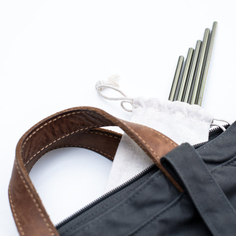 Set of stainless steel reusable straws in a drawstring pouch spilling out of a bag
