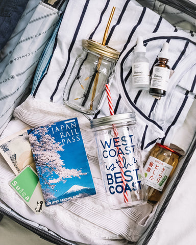 close up shot of carry on suitcase with travel documents and glass mason jar tumblers