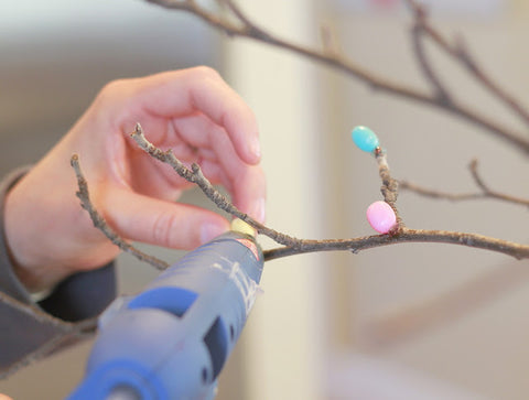 Woman hot gluing pastel colored jelly beans on to twigs to make an Easter tree from Crafty Sisters