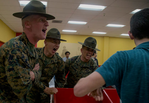 Three Marine Corps drill sergeants yell at a recruit.