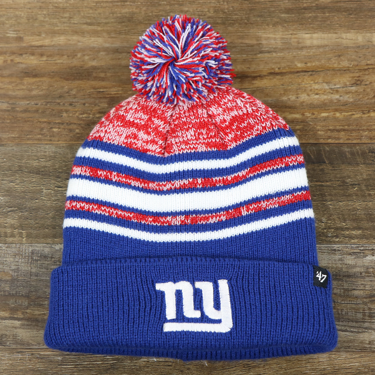 The front of the Kid’s New York Giants Striped Pom Pom Winter Beanie | Royal Blue, Red, And White Beanie