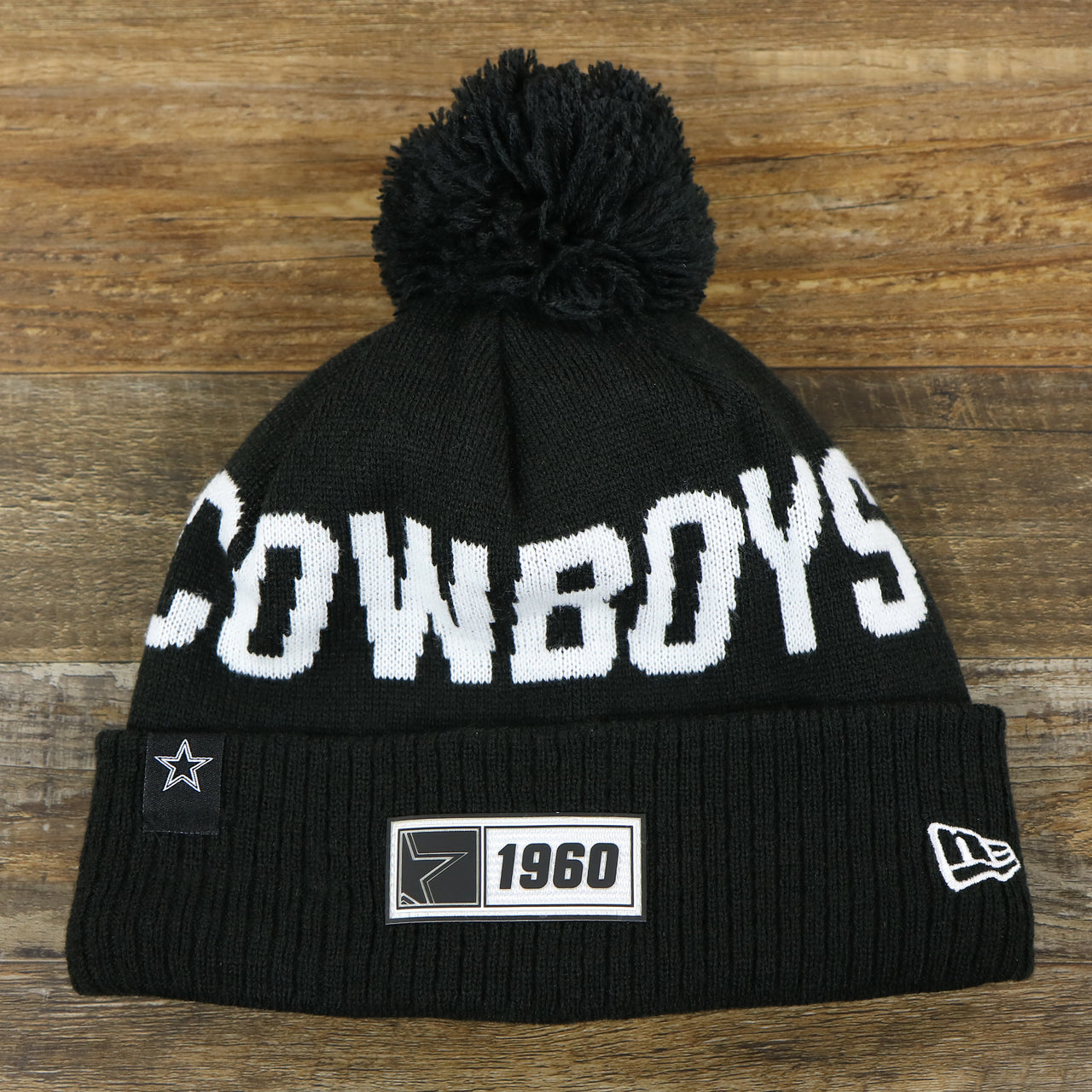 The front of the Dallas Cowboys On Field Rubber Cowboys 1960 Patch Cuffed Pom Pom Winter Beanie | Black Winter Beanie