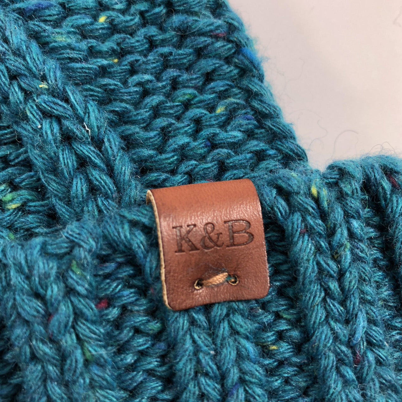 on the raised cuff of the women's teal cable knit beanie is a brown leather kb label