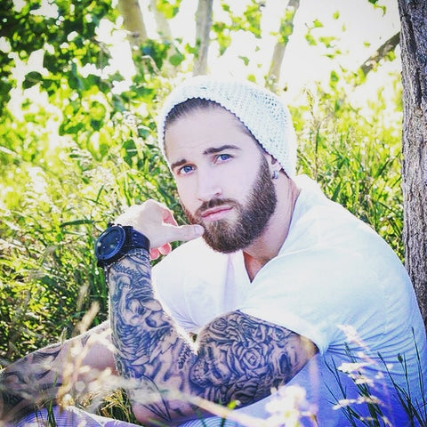 Lumbersexual (hipster, metrosexual with a beard) wearing a beanie with a Treehut wood watch and floral tattoos