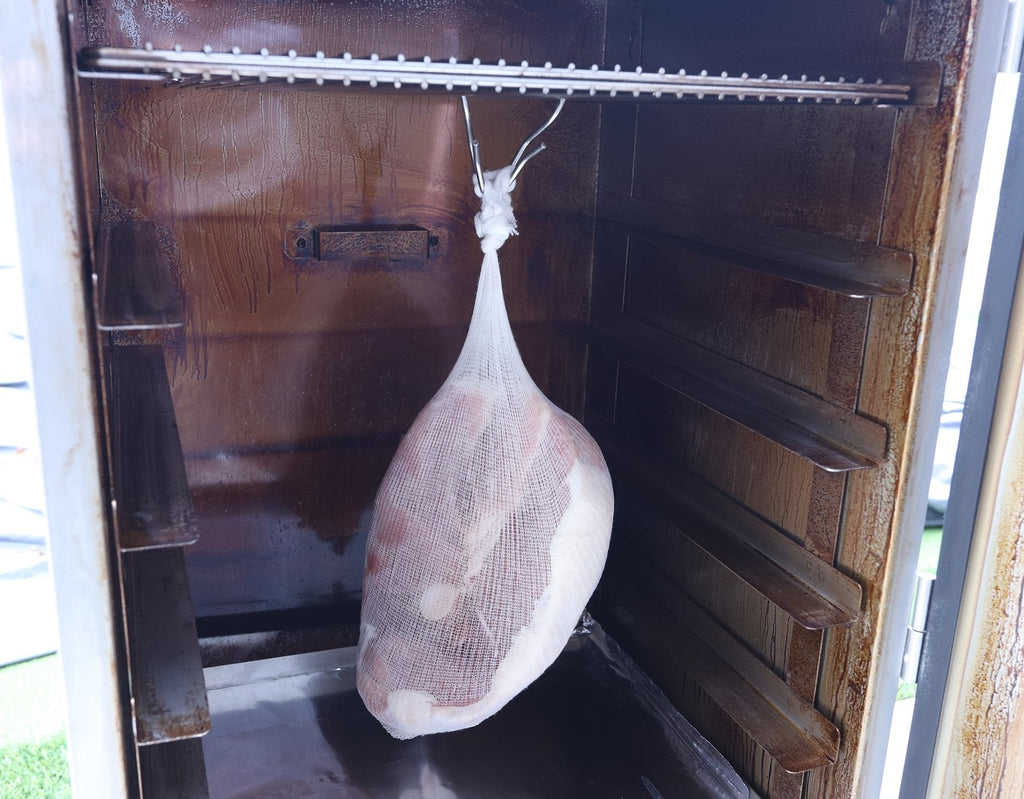 cured ham hanging in a smoker