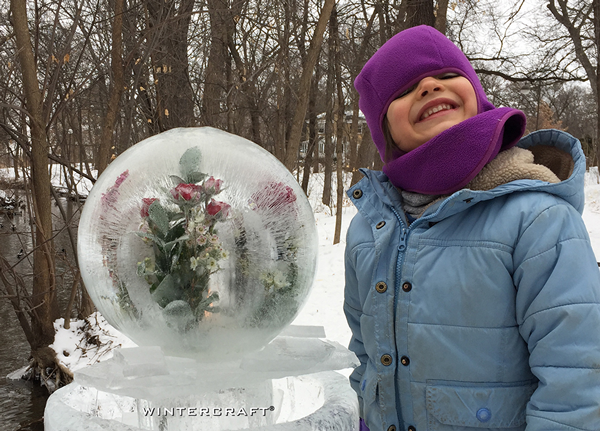 Young helper at the 2018 Middlemoon Creekwalk standing next to a giant globe with flowers inside Wintercraft