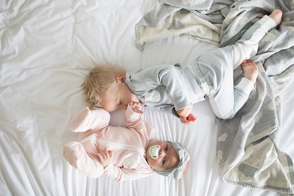 toddler brother and baby sister playing on bed together