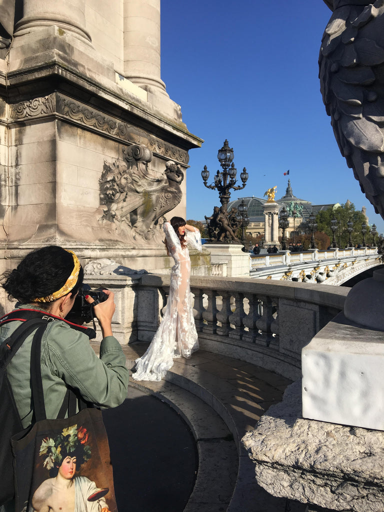 Photographer taking a photo of model posing in wedding dress on a bridge in paris.