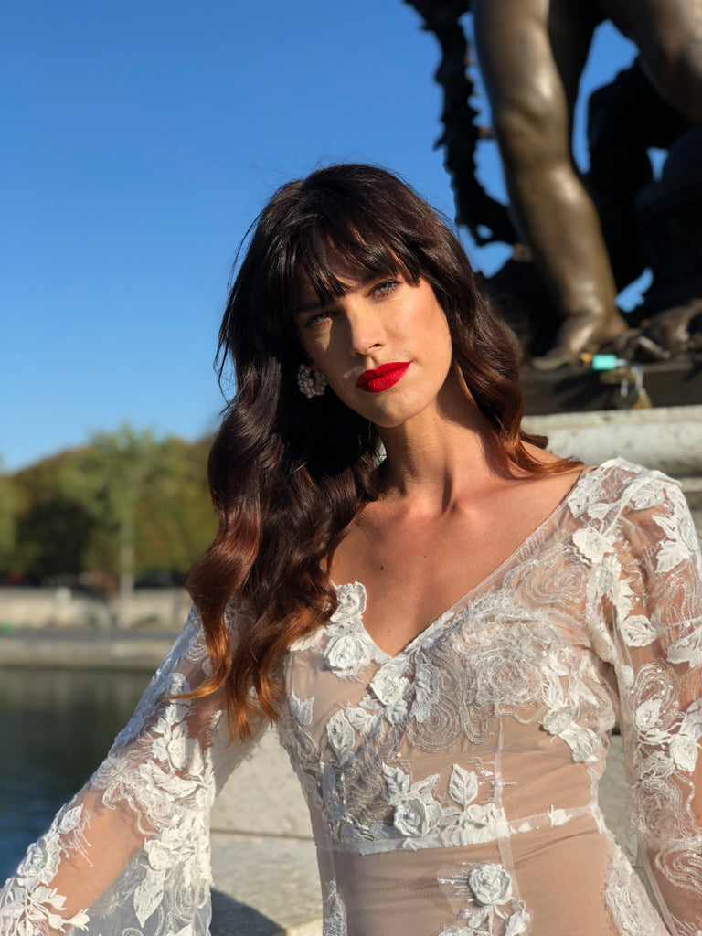 Model in red lipstick posing in a wedding dress on Pont Alexander bridge in Paris.