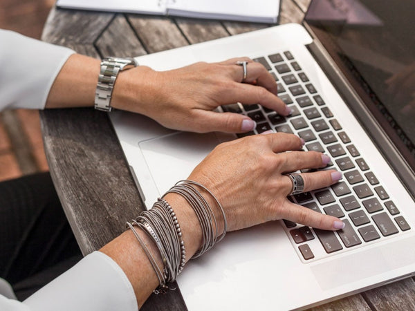 woman working on her laptop wearing bracelets and rings