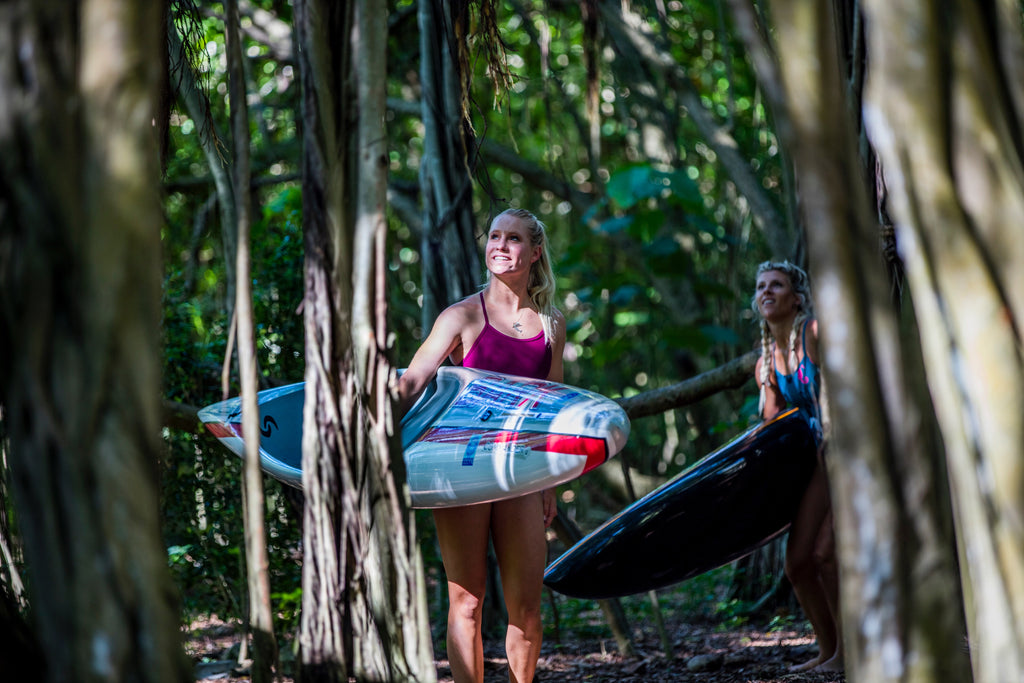 Charger Carter and friend walking with surfboards through a forest