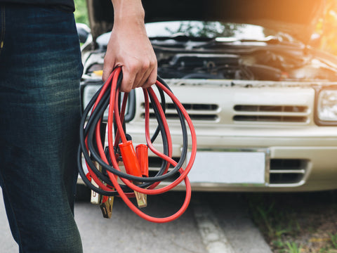 man holding jumper cables with broken down car in background
