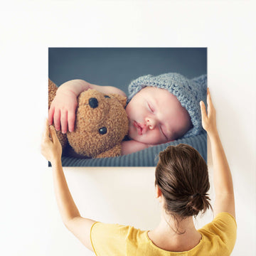 A woman is holding and sizing up a large 'Create Your Own' metal poster display plate print she has made from a photo of her cute baby cuddling a teddy bear