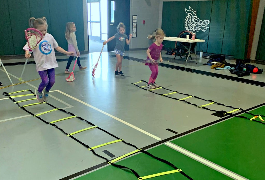 Lacrosse players practice running through the ladder while cradling.