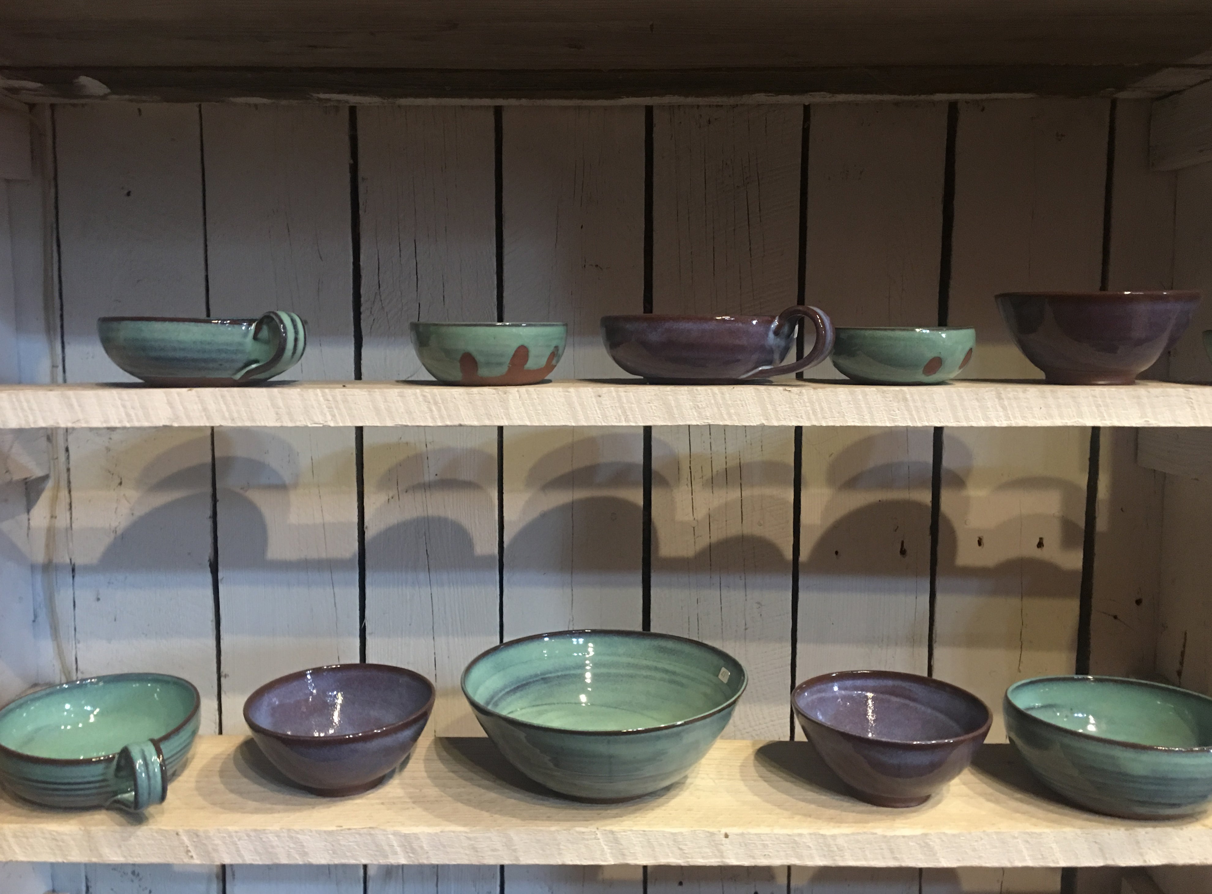 Green and purple bowls sit on shelves at Greenbridge Pottery Studio