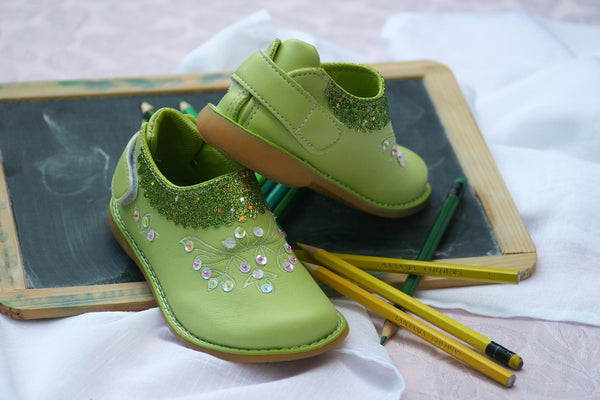 Image of children's green shoes sitting atop a toy blackboard and some pencils