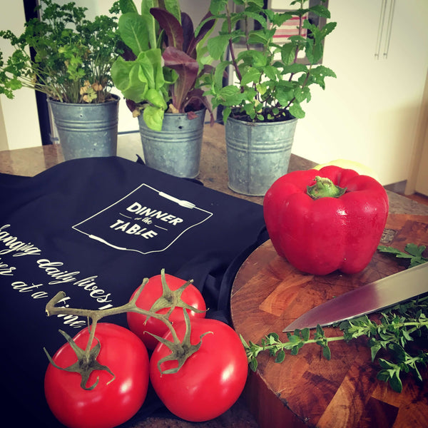 Image of vegetables on a chopping board, apron, knife and potted herbs