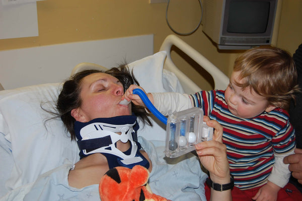 Marjorie lying in a hospital bed with her son assisting her with breathing exercises