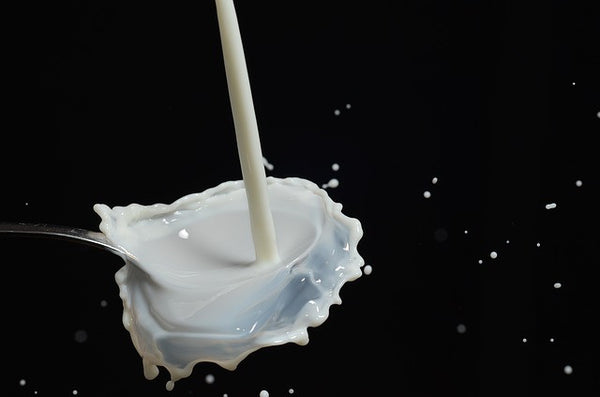 Image of milk spilling into a spoon on a black background