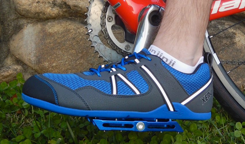 Side view of a Blue Catalyst Pedal and Xero Prio athletic shoe with grass and stonework in the background.