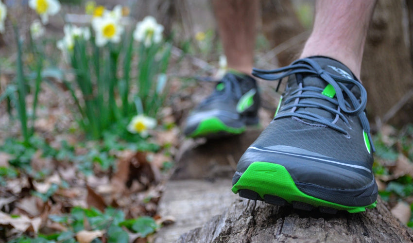 Runner wearing Altra athletic shoes balancing on a log in springtime conditions